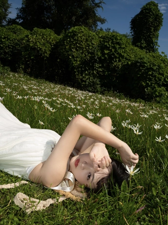 一位穿着白色连衣裙的年轻女子躺在草地上的花丛中。