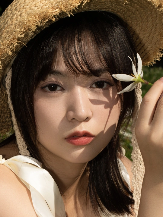 一位年轻女子戴着草编帽子 手里拿着一朵白花。