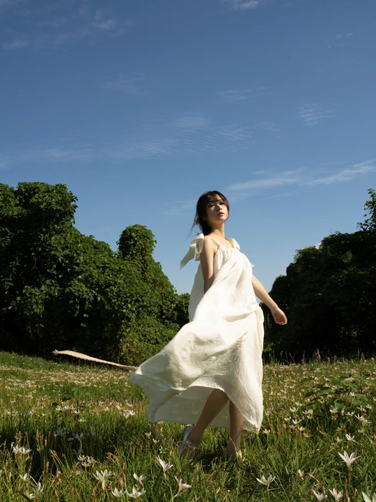 一位穿着白色连衣裙的年轻女子穿过一片绿色田野