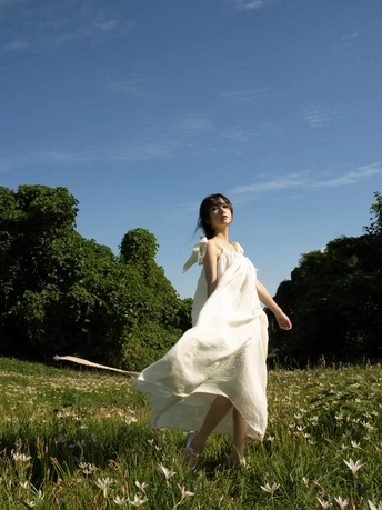 一位穿着白色连衣裙的年轻女子穿过一片绿色田野
