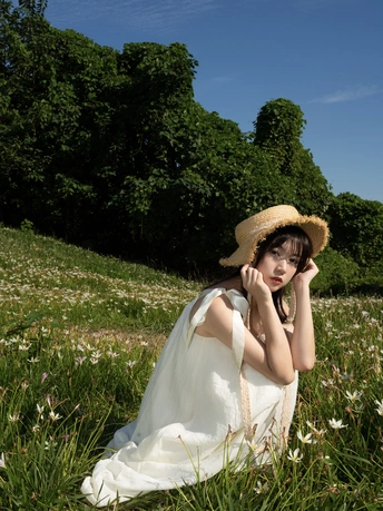 一位穿着白色连衣裙和草编帽子的年轻女子坐在一片白色花朵的草地上。