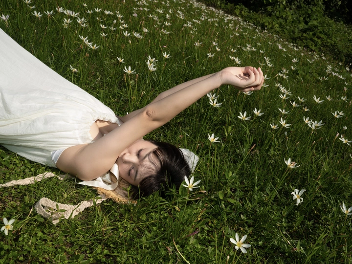 一位穿着白色连衣裙的年轻女子躺在草地上的花丛中。