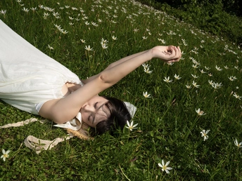 一位穿着白色连衣裙的年轻女子躺在草地上的花丛中。