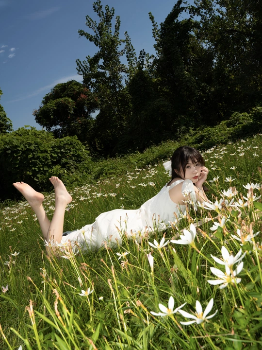 一位穿着白色连衣裙的年轻女子躺在草地上的花丛中。