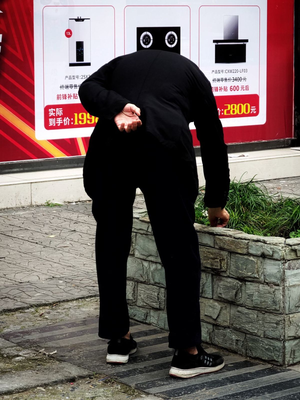 一个穿黑色西装的男人靠在墙上看着人行道上的一块告示牌