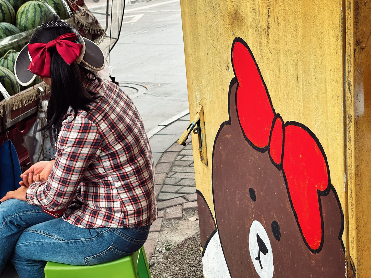 一个年轻女子坐在人行道旁的一把绿色椅子上 旁边有一堆西瓜。