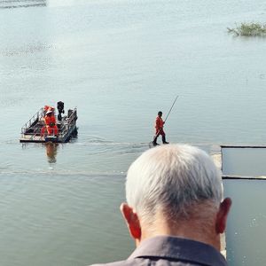 一个小船上站着一个男子 正在注视着在一片水域中钓鱼的人们。