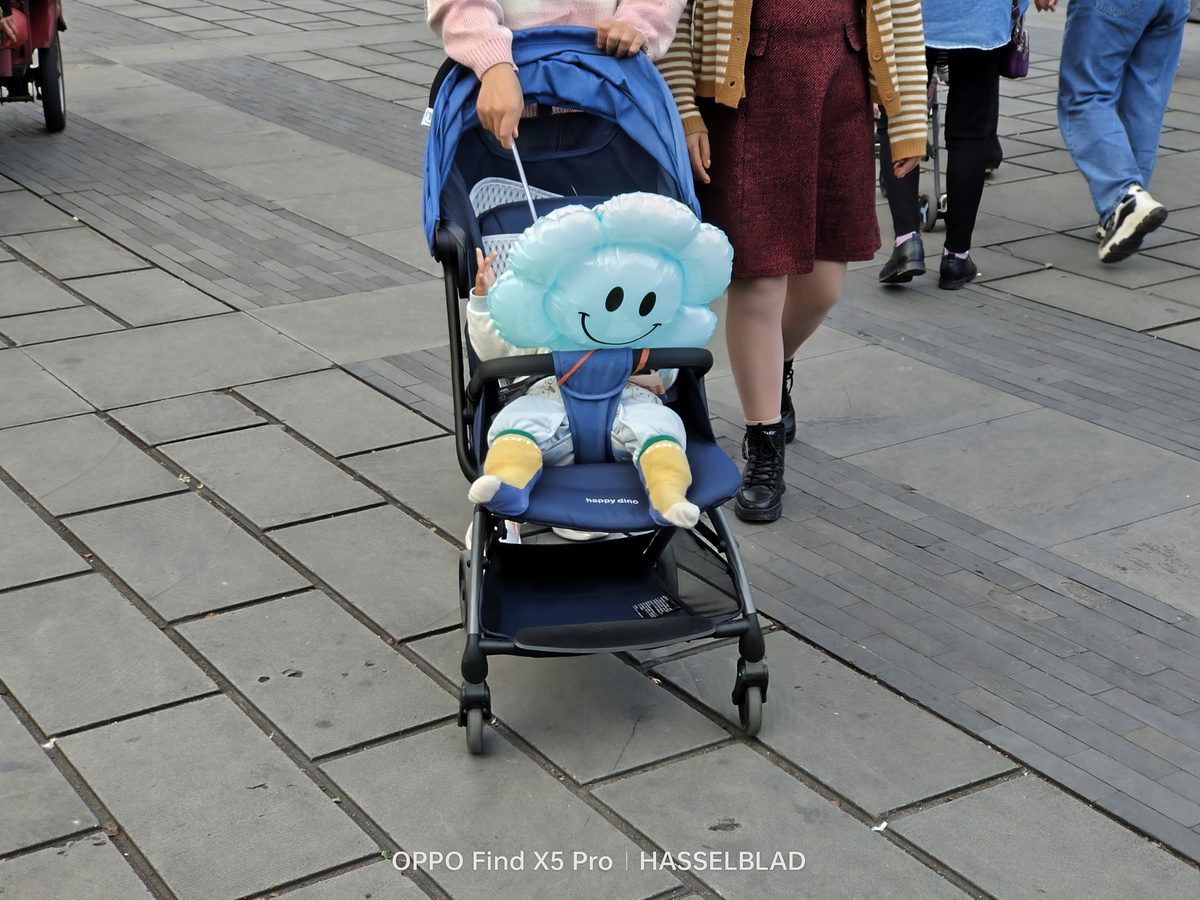 一位女士推着装有蓝色泰迪熊的小推车和一个小孩子 人们走在人行道上。