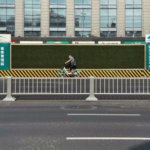 一个人骑自行车在有围栏和障碍物围绕的街道上 路边有一块告示牌。