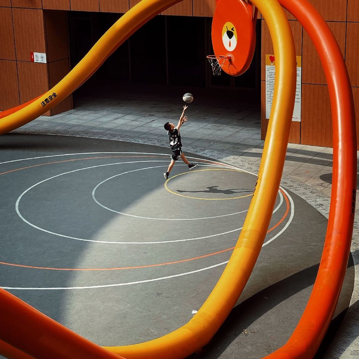 一个年轻人在操场上和一个小男孩在场上打篮球