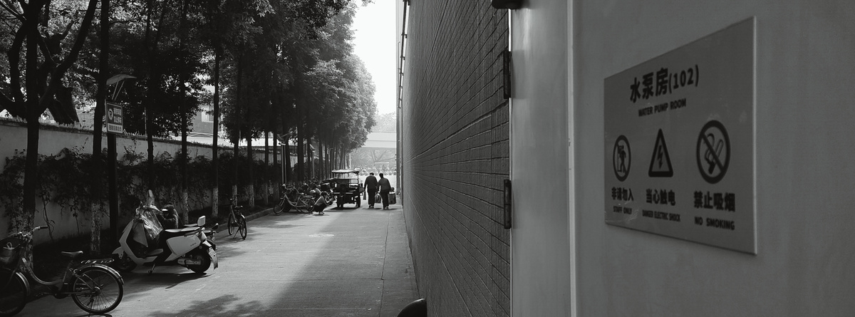 人行道上的黑白照片 有行人、摩托车、自行车和树木。
