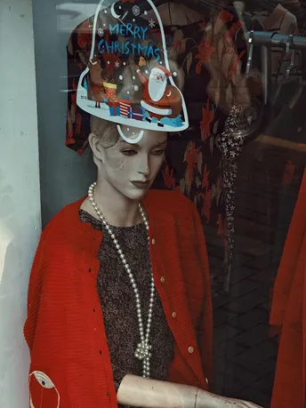 一位穿着红色夹克和帽子女士正在商店橱窗前看着一个模特。