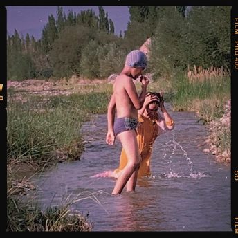 一个穿着泳衣的男孩在溪流中玩耍 同时一个妇女、一个年轻女子和一个年轻男子在水中走动。