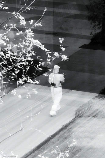 一张黑白照片 一位男士站在人行道上 前方有一扇窗户 手里拿着一把伞。