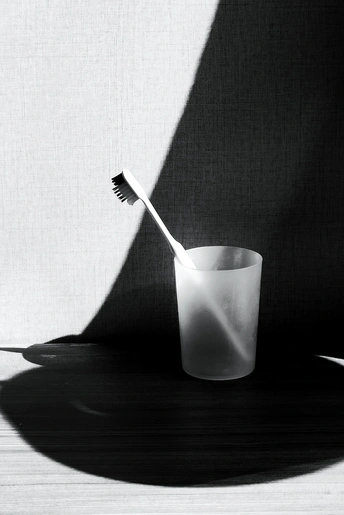 一支牙刷放在一个白色的杯子上 桌子上有黑白相间的阴影。