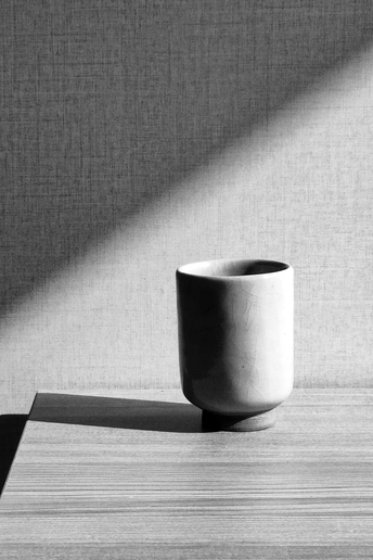 一个白色的咖啡杯放在桌子上 投射出光线在桌子上形成一个阴影。