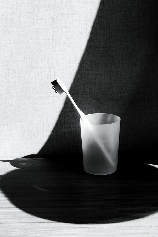 一支牙刷放在一个白色的杯子上 桌子上有黑白相间的阴影。