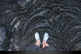 一个人站在一个黑色的海滩上 双脚在水中 鞋在沙子上