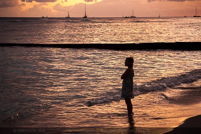 一个小女孩站在夕阳下 临近海洋的海滩上。