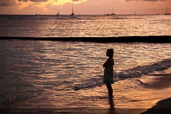 一个小女孩站在夕阳下 临近海洋的海滩上。