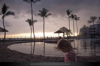 一个小女孩站在一片水坑里 面向落日 凝望着海洋。