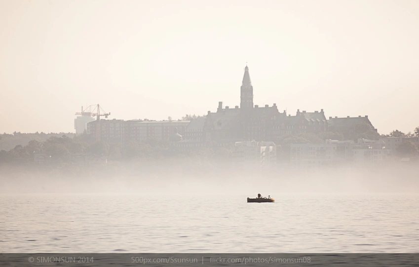 雾气笼罩的城市中 一艘小船漂浮在一大片水域上。