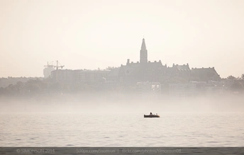 雾气笼罩的城市中 一艘小船漂浮在一大片水域上。