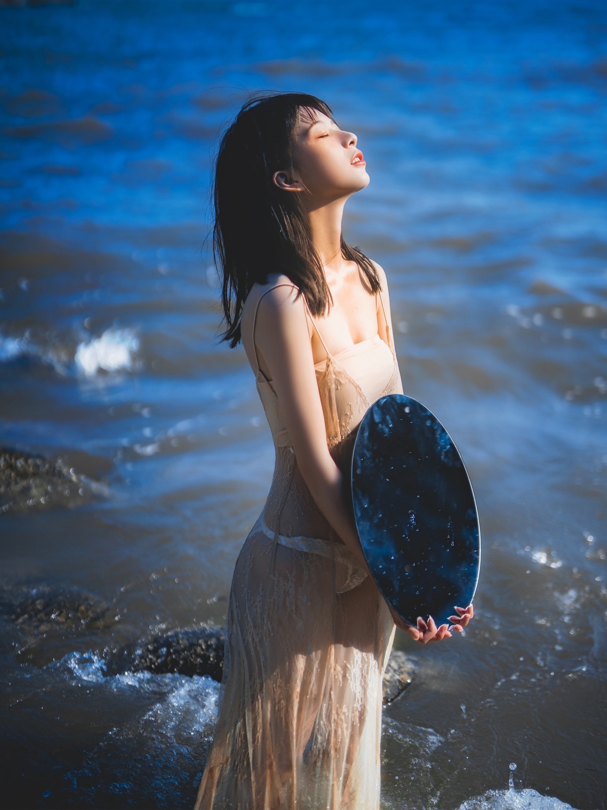 一个穿着蓝色连衣裙的美丽年轻女子站在海滩的水中