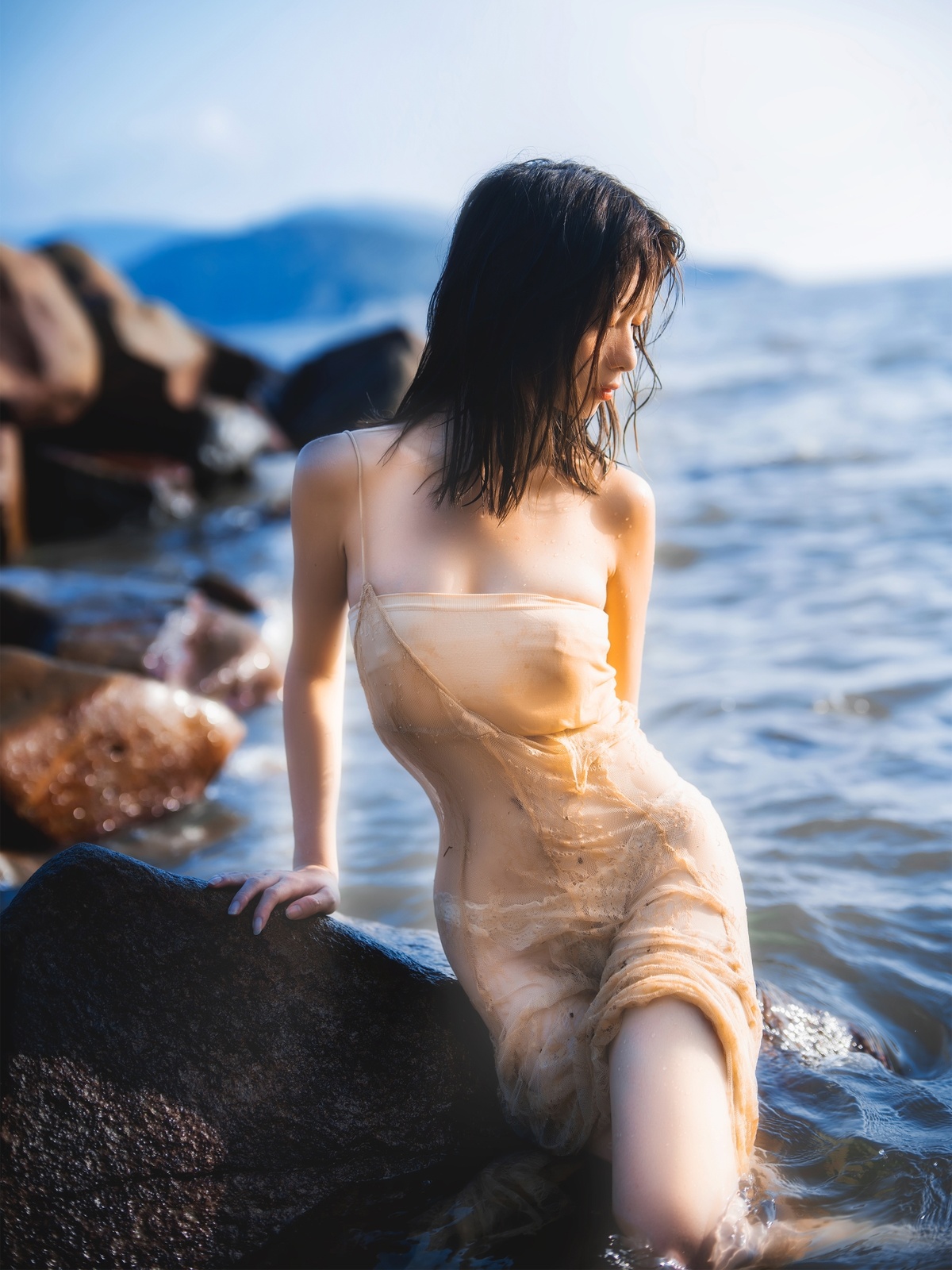 一个穿着漂亮连衣裙的年轻女子坐在水中的岩石上