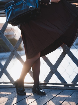 一位穿着黑色裙子和黑色鞋子 拿着蓝色钱包站在桥上 背景是围栏的女人