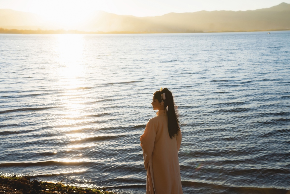 一位年轻女子站在海滩的岸边 看着夕阳下的海洋。