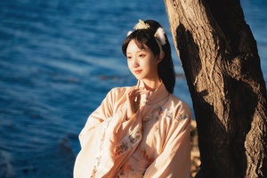 一位穿着日本传统服装的年轻女子站在海边的沙滩上 靠近一棵树。
