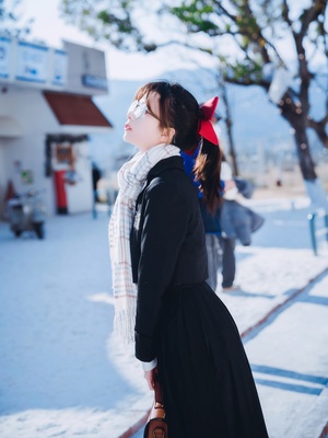 一个穿着黑色连衣裙 头戴红蝴蝶结的年轻女子走在一条铺满雪的街道上。