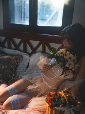 一位年轻女子抱着白色花朵坐在床上