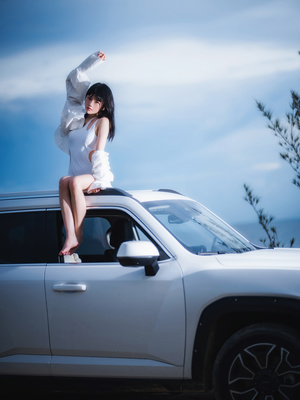 一个年轻女子坐在一辆白色汽车的车盖上