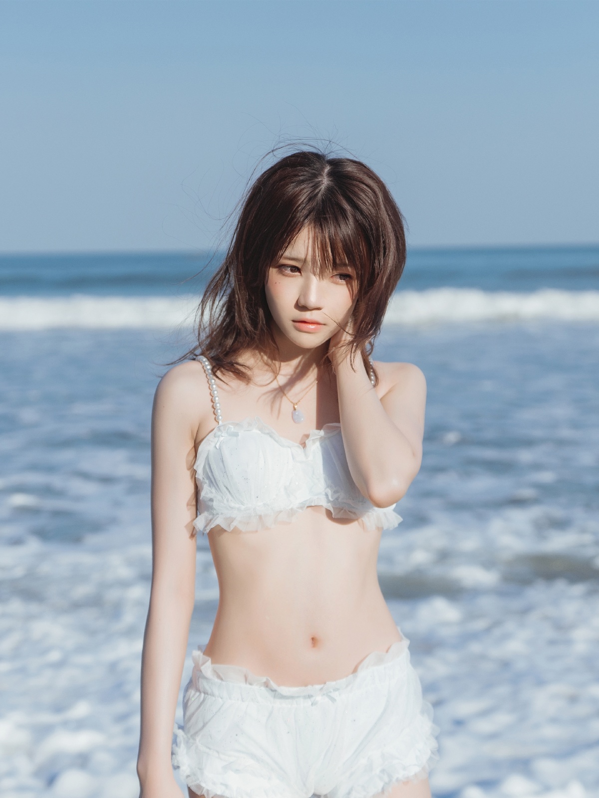 一位穿着白色比基尼的年轻女子站在靠近海洋的海滩上