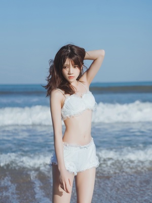美丽的年轻女子穿着白色比基尼在海滩上为海景拍照
