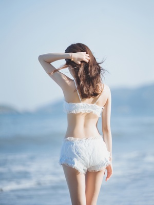 一位穿着白色比基尼的年轻女子站在海滩附近的海边