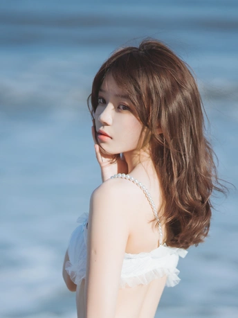 一位长发白衣少女站在海滩附近的水边