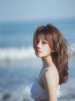 一位穿着白色连衣裙的年轻女子站在海滩附近的海边 海面波光粼粼。