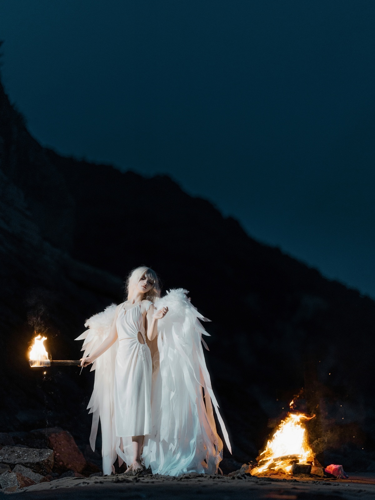 夜晚篝火旁穿着天使装的一个女人 手持火炬。