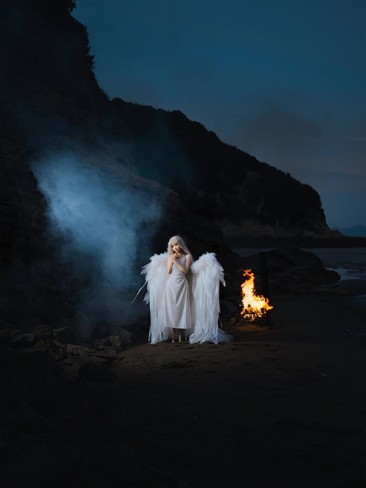 一位穿着天使装站在夜晚海滩边的篝火旁的女子