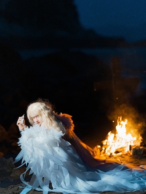 一位穿着白色连衣裙的年轻女子晚上坐在海滩上的篝火旁 看着一个小女孩。