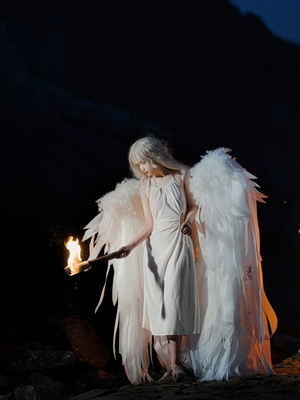 一个穿着白色翅膀和白色连衣裙的女人 手里拿着一支蜡烛 空中燃着火焰 夜晚。