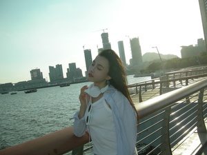 一位年轻女子站在桥上喝着水 背景是一个城市。