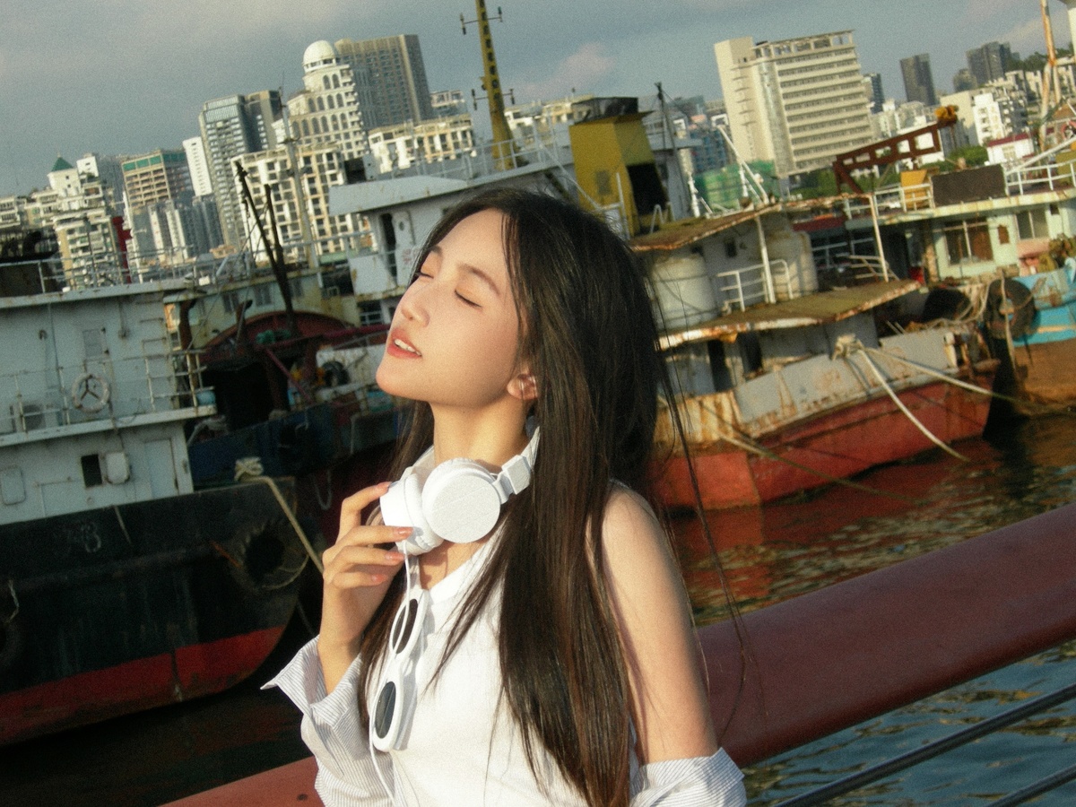 一个戴白色耳机的女青年站在一艘船上听音乐