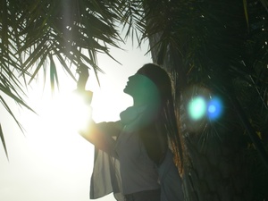 在一棵棕榈树下 一个人站在那里 阳光透过树照射下来 另一个人手里拿着灯。