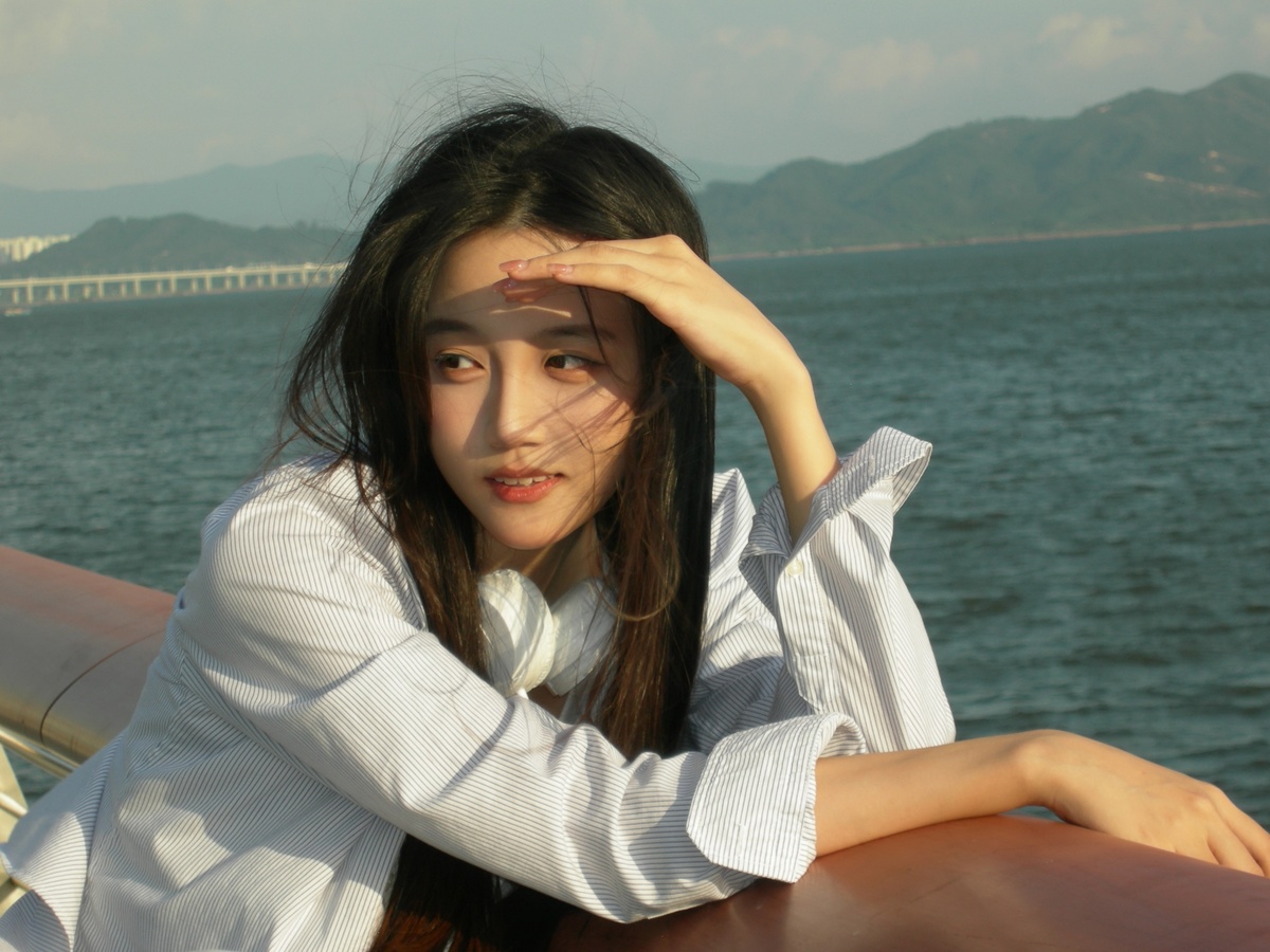 一位穿着白色衣服的年轻女子在一艘船的中间 背景是海上的桥和水。