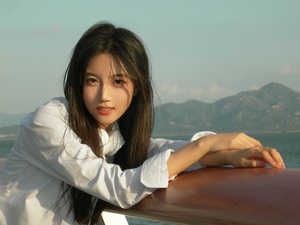 一位穿着白衬衫的年轻女子倚靠在阳台的围栏上 眺望着海洋和海面。