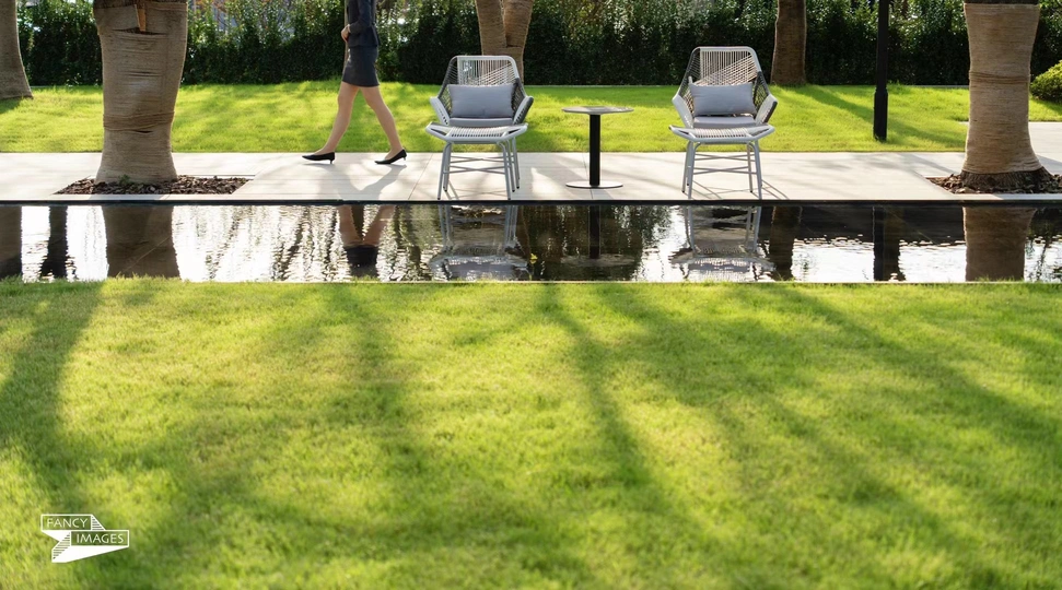 一位站在棕榈树附近的游泳池草坪上的女人 手里拿着一把伞 旁边还有一个人在草地上走。